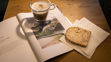 Un livre, une tasse de café et une tranche de pain sont posés sur une table, et une photographie se trouve à proximité.