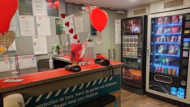 A reception desk with a sign encouraging social distancing, a vending machine with snacks, and a wall with various informational posters. - hotelF1 Beauvais (Beauvais)