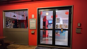 A hotel entrance with a red wall, a welcome mat, and a digital information board. - hotelF1 Beauvais (Beauvais)