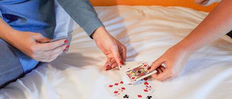 A person holding playing cards on a bed with white sheets.