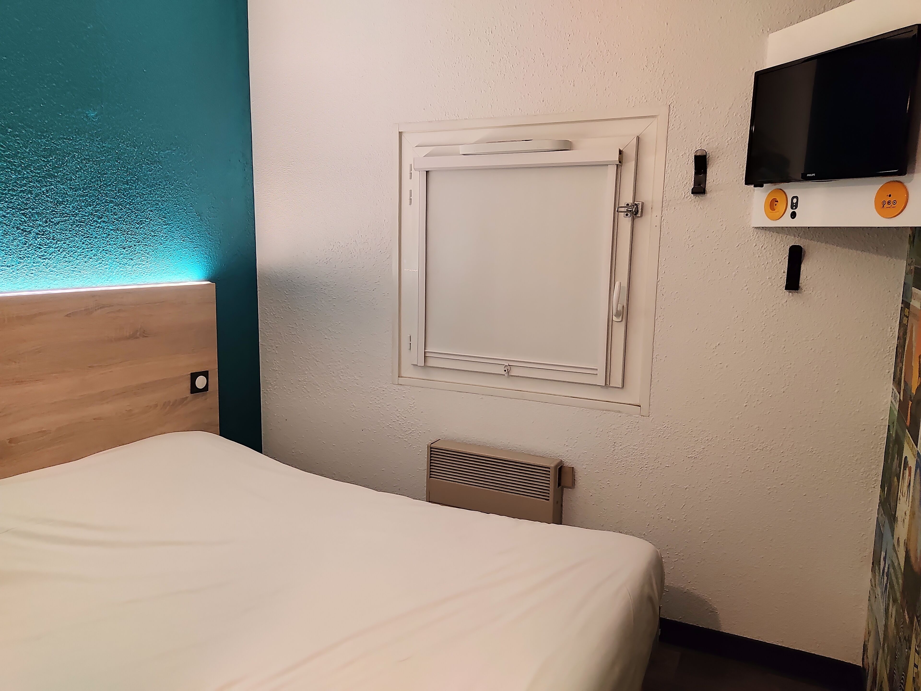 Een hotelkamer met een bed, een tv aan de muur en een kleine airconditioning.