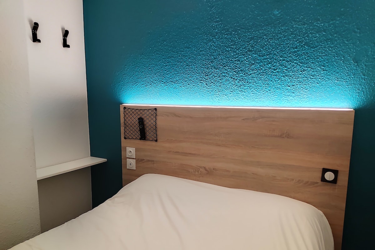 A bedroom with a wooden headboard, a white bed, and a shelf with two black hooks.