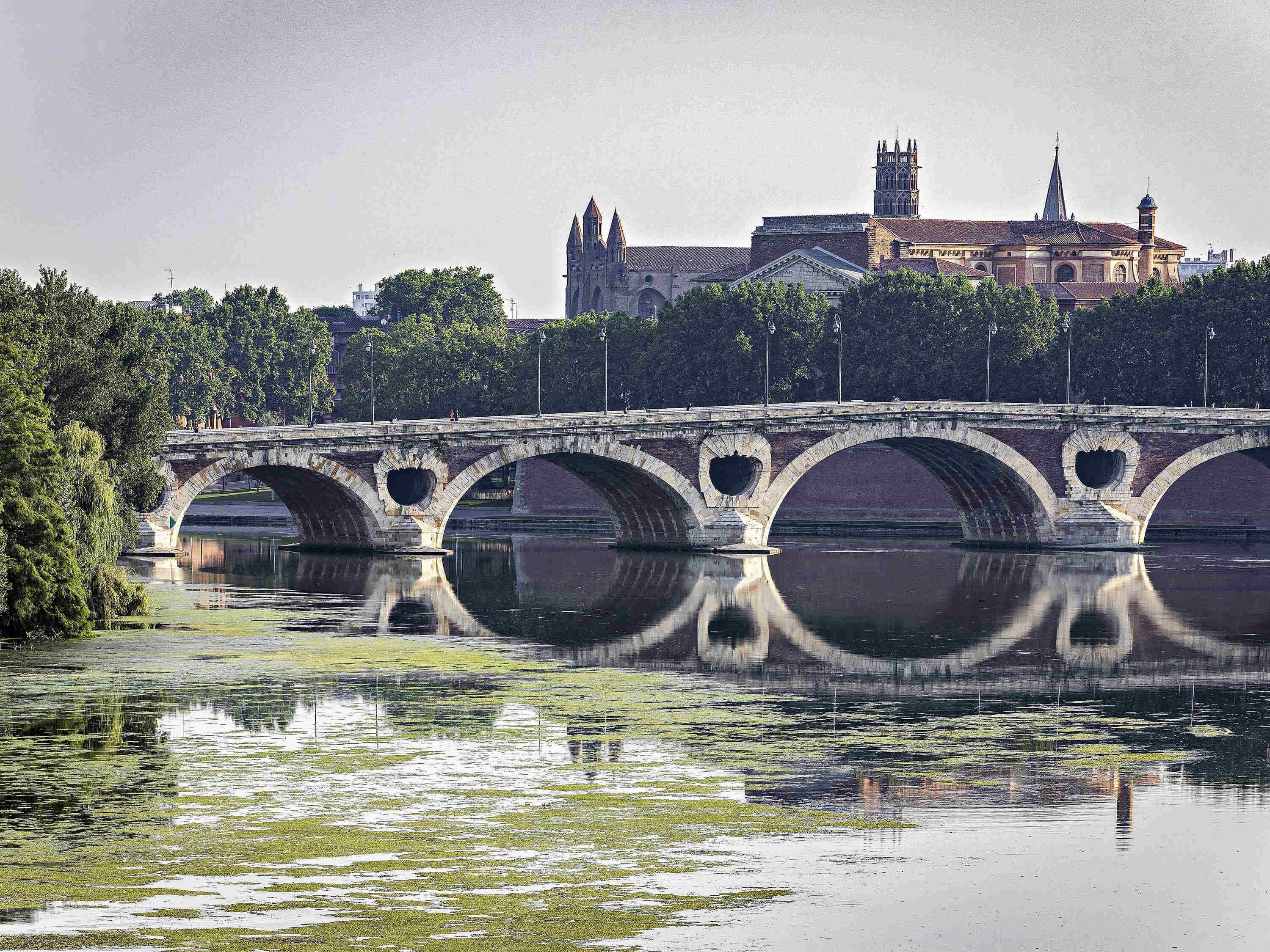 Eine Steinbrücke über einem ruhigen Fluss, im Hintergrund ein historisches Gebäude.