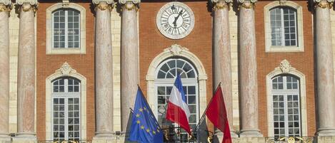 A building with the word 'CAPITOLIUM' above a clock, flanked by columns, and flags of the EU and France.