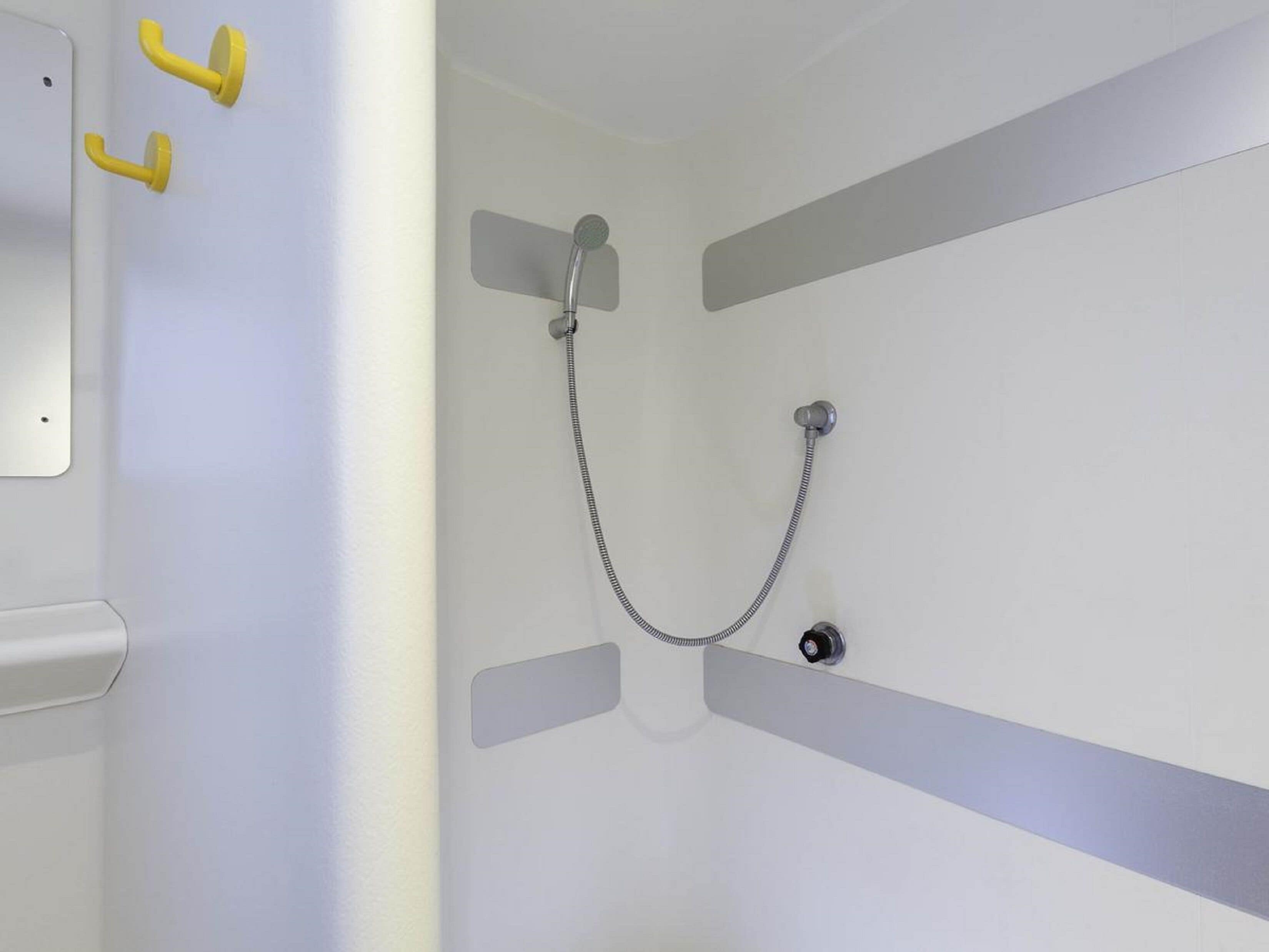 Ein Badezimmer mit Dusche, Toilette und zwei gelben Handtuchhaken.