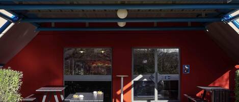A hotel entrance with a red facade, a yellow sign reading 'hotelFL.com', and a covered outdoor seating area with tables and benches.