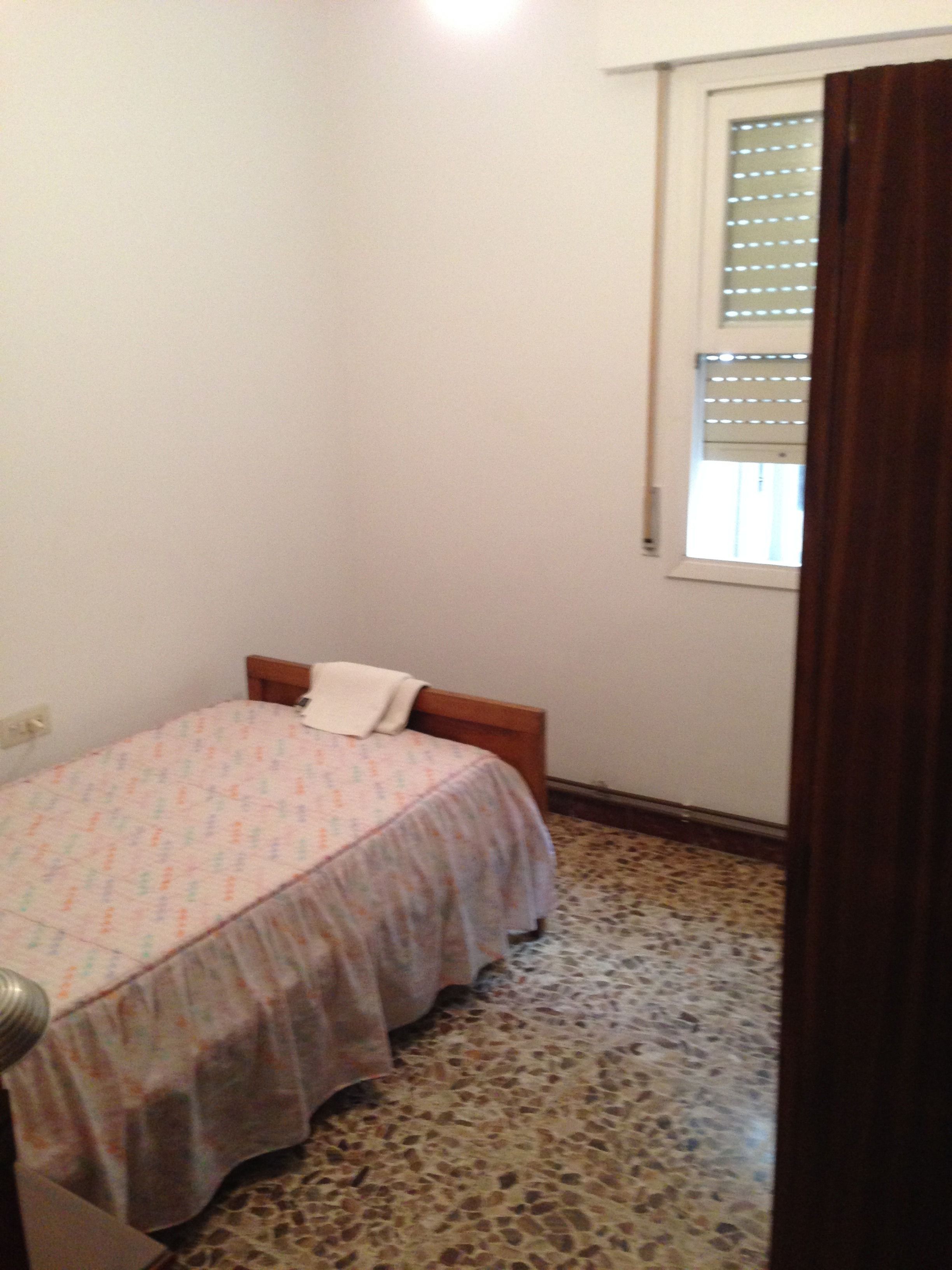 A small bedroom with a single bed, a window with blinds, and a patterned floor.