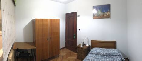 Un dormitorio con un armario de madera, una cama con ropa de cama estampada, una mesita y una silla.