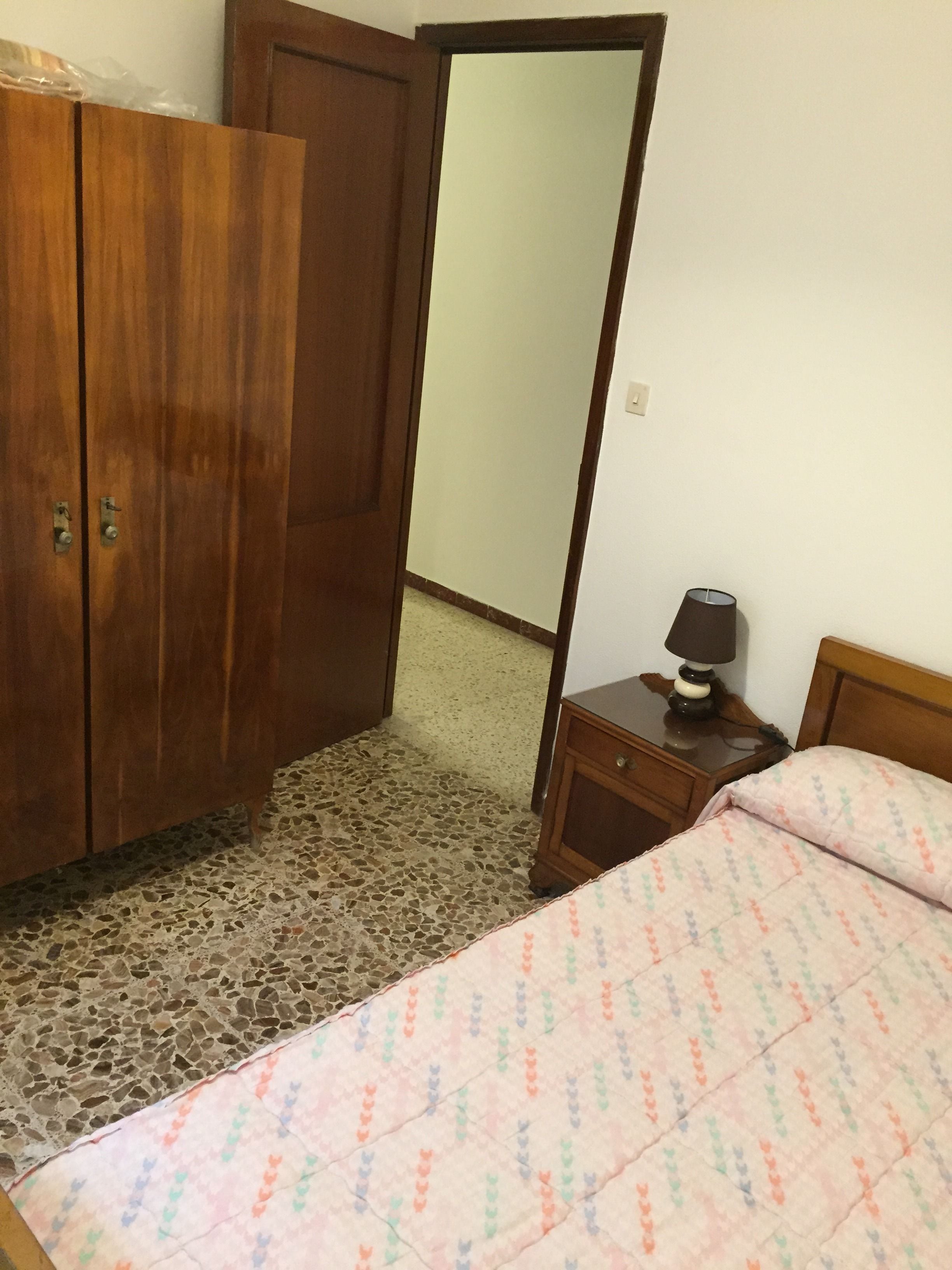 A bedroom with a bed, a nightstand, a lamp, a wardrobe, and a mirror.