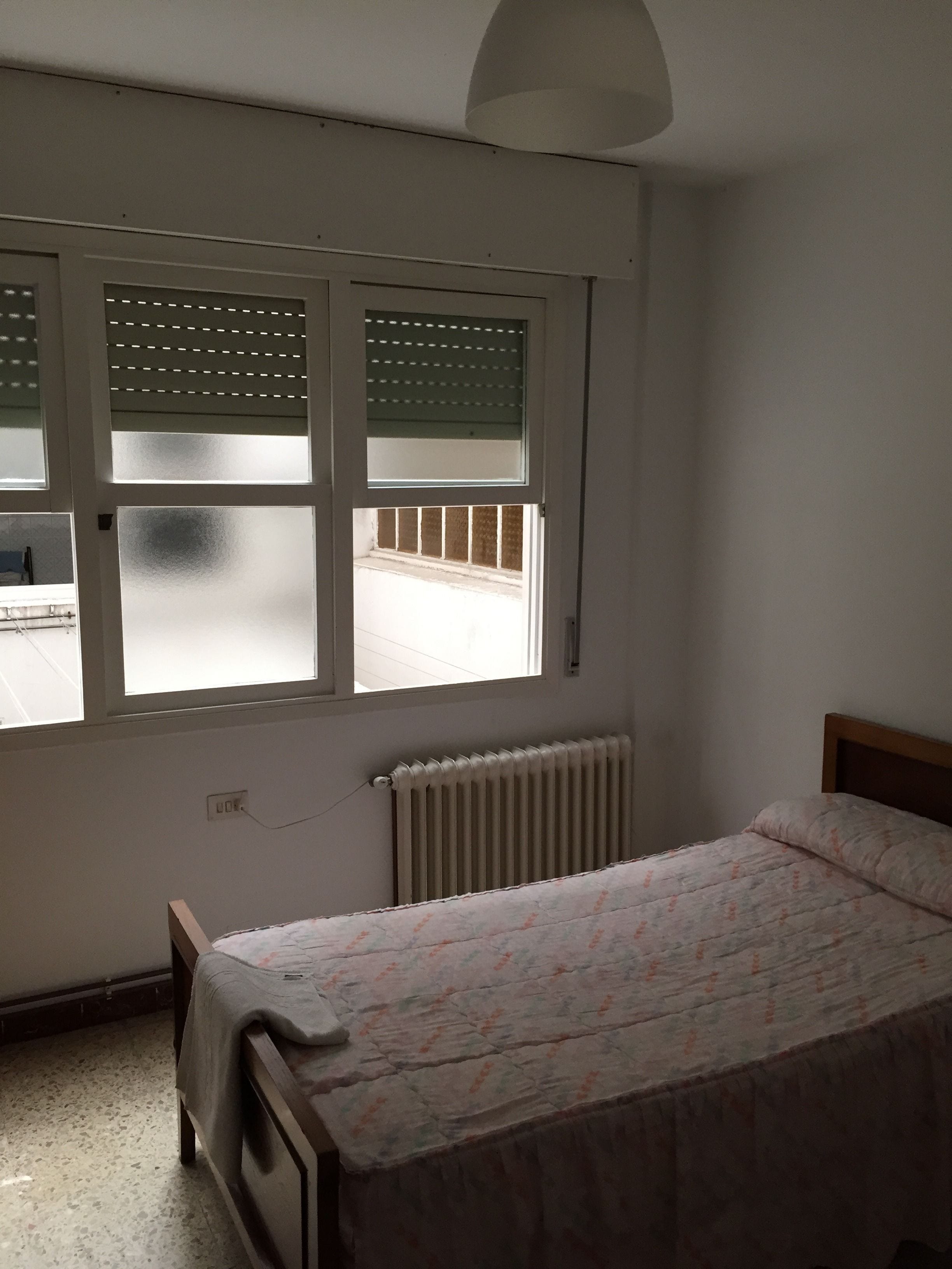 Una camera da letto con un letto, un termosifone e una finestra con persiane.