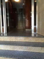 Una escalera de mármol que conduce a una puerta de madera, con una lámpara colgante arriba.