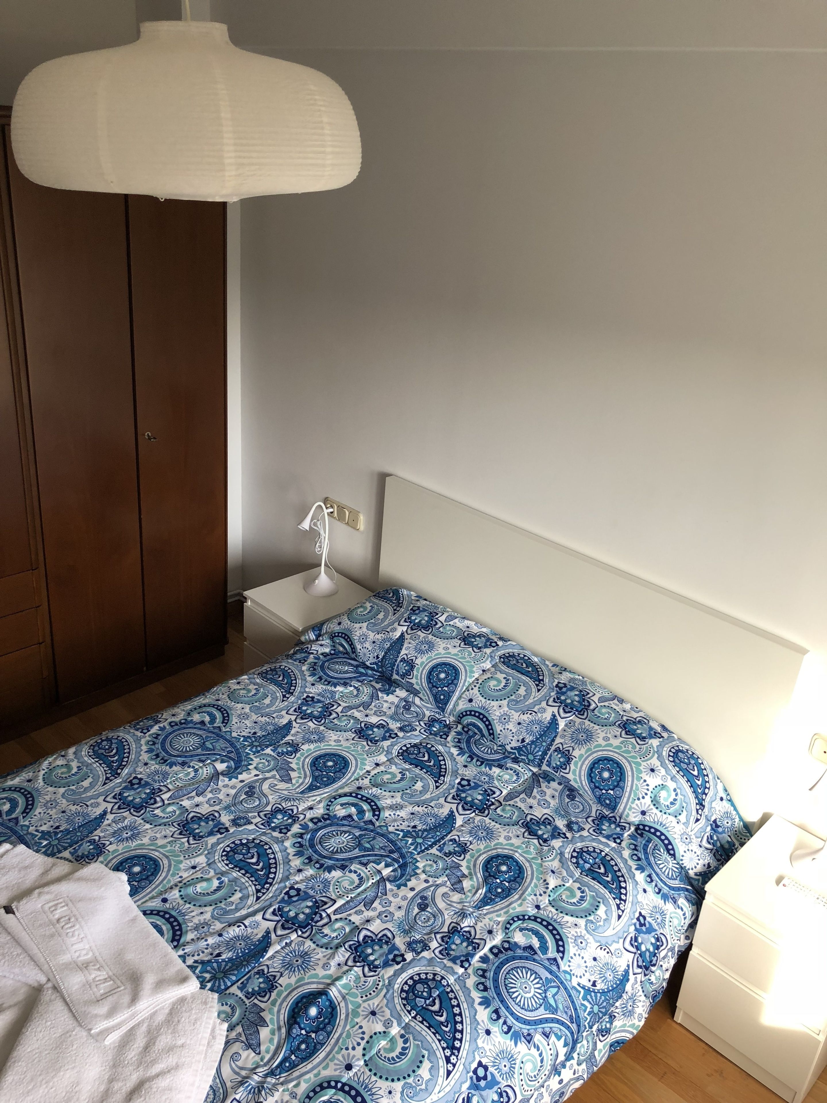 Ett sovrum med en säng, ett nattduksbord, en sänglampa, en garderob och en hängande taklampa.