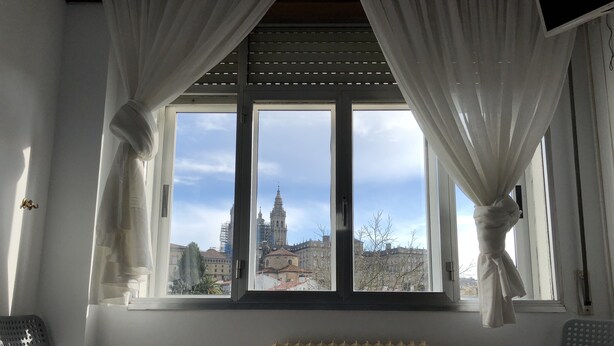 A room with a large window, white curtains, a radiator, and two chairs. - Hostal Costa Azul (Santiago de Compostela)