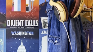 Una chaqueta vaquera con auriculares colgados en una pared con varios carteles de viaje.