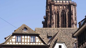 Un edificio histórico con una torre destacada y casas tradicionales adosadas con entramado de madera.