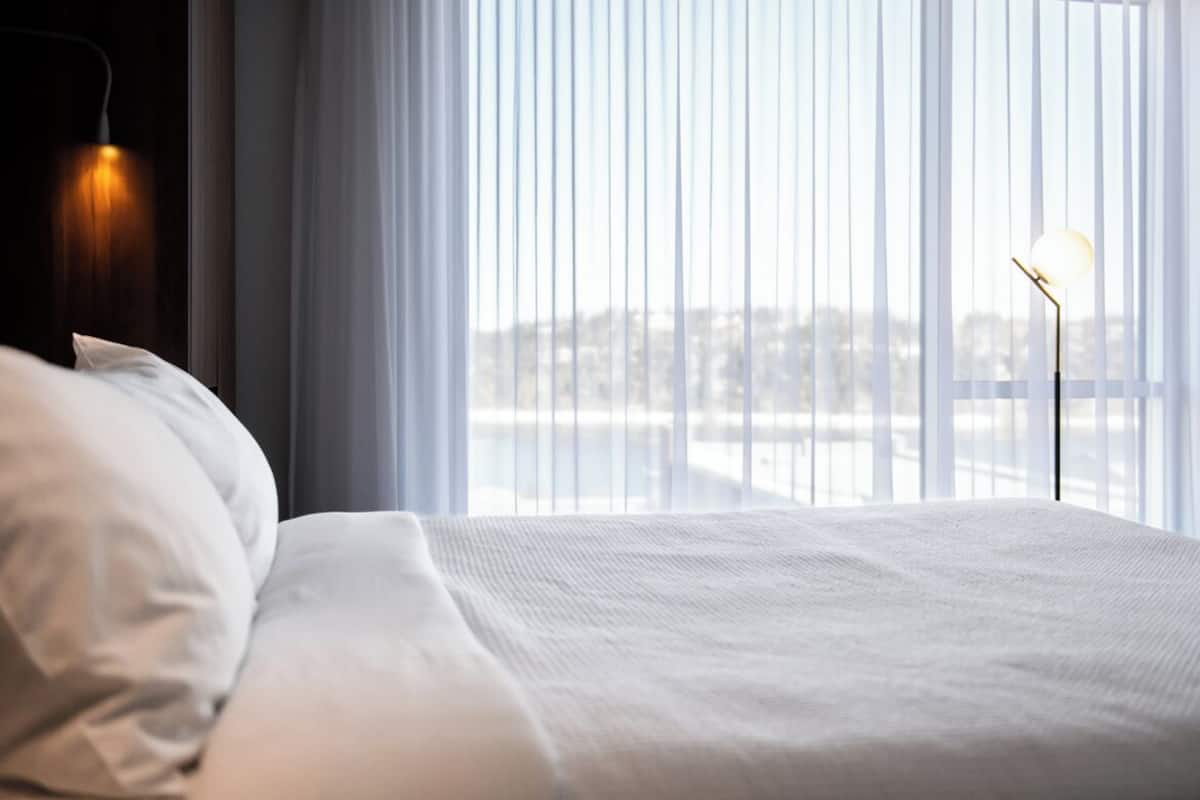 Ein Hotelzimmer mit Bett, Nachttischlampe und Blick durch transparente Vorhänge.