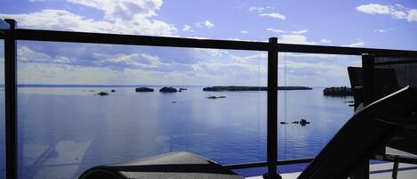 A balcony with a clear view of a calm body of water, a chair, and a railing.