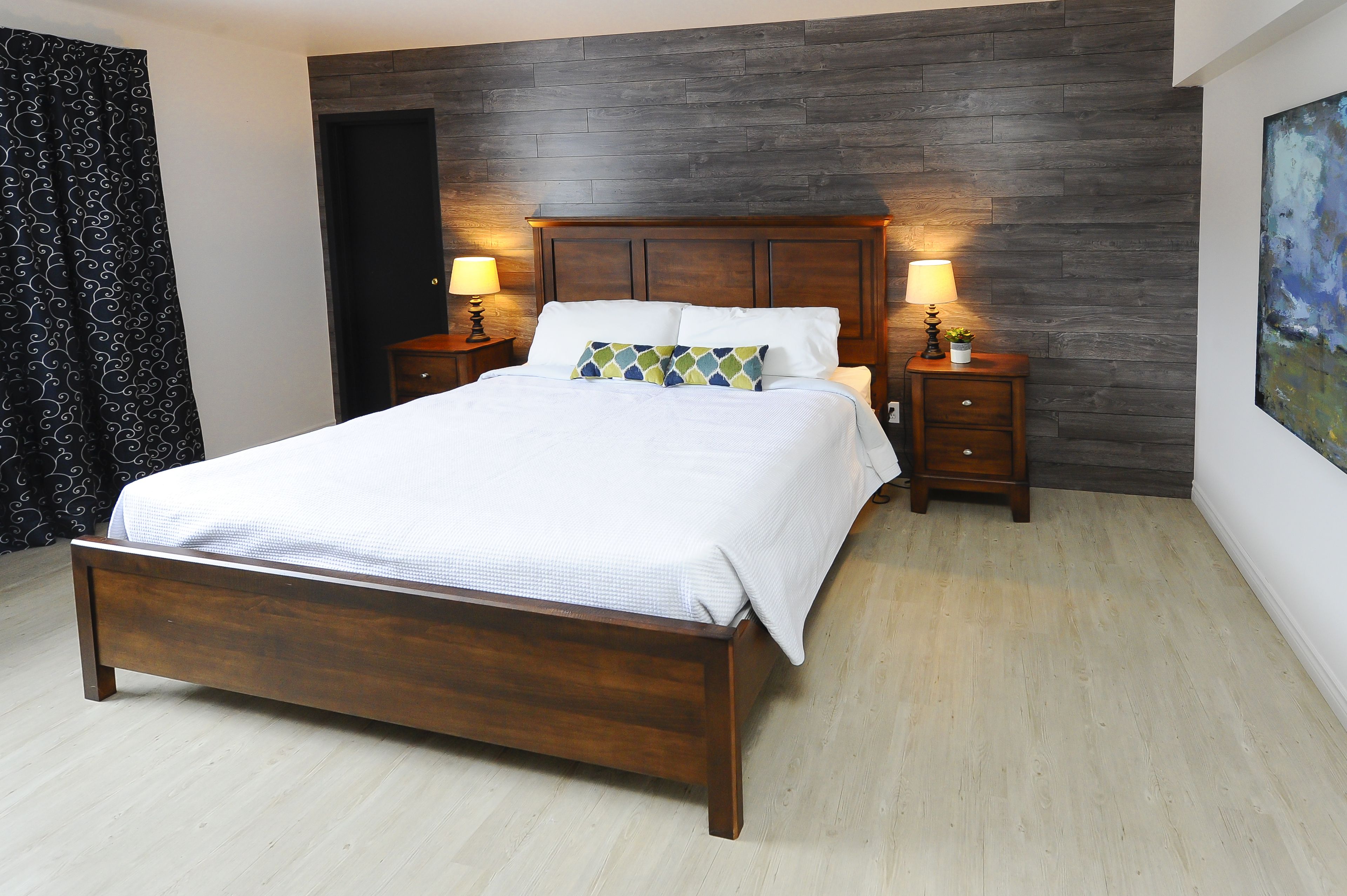 Une chambre à coucher avec un lit en bois, deux tables de chevet avec des lampes, une tête de lit en bois foncé et un plancher de couleur claire.