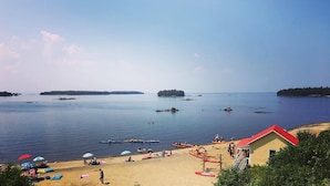 A beach with kayaks, a sandy shore, and a building with a red roof. - Auberge des Îles (Saint-Gedeon)