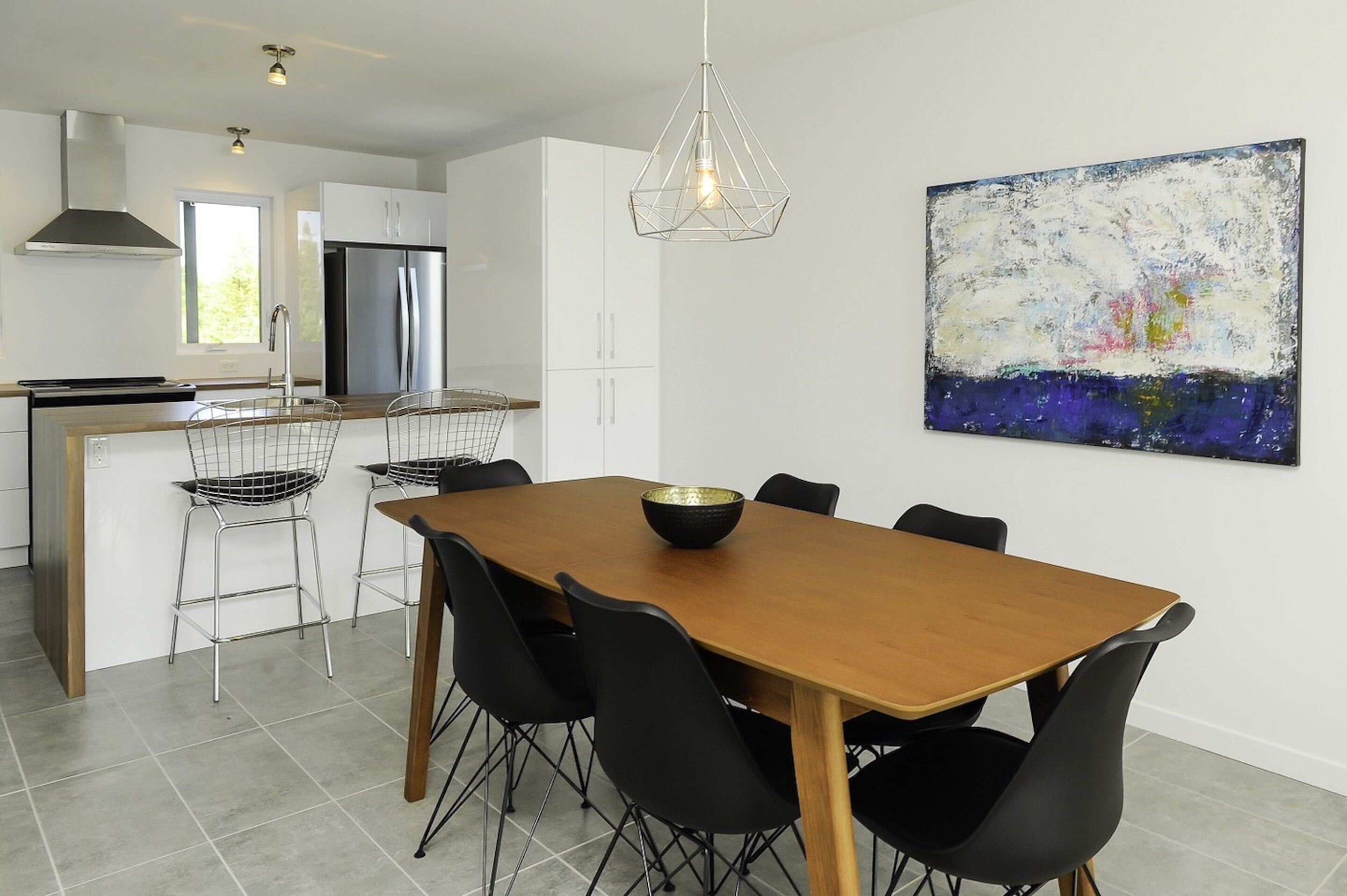 A modern kitchen with white cabinets, a stainless steel refrigerator, and a dining area with a wooden table and black chairs.