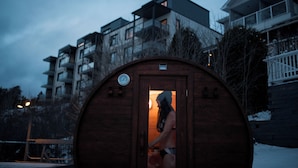 A wooden sauna structure with a door, surrounded by residential buildings. - Auberge des Îles (Saint-Gedeon)
