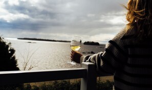 A person holding a glass of white wine, overlooking a body of water with a cloudy sky. - Auberge des Îles (Saint-Gedeon)