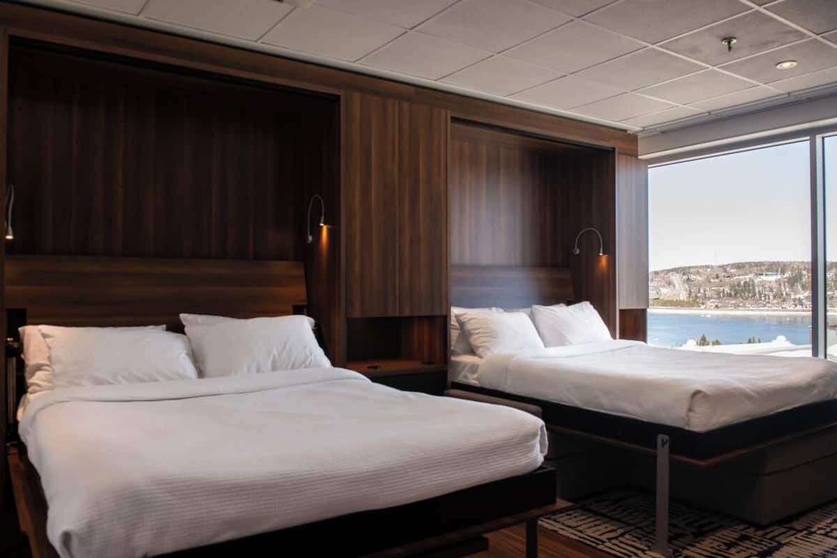Ein Hotelzimmer mit zwei Betten, einem großen Fenster mit Blick auf die Stadt und einem Holzkopfteil.