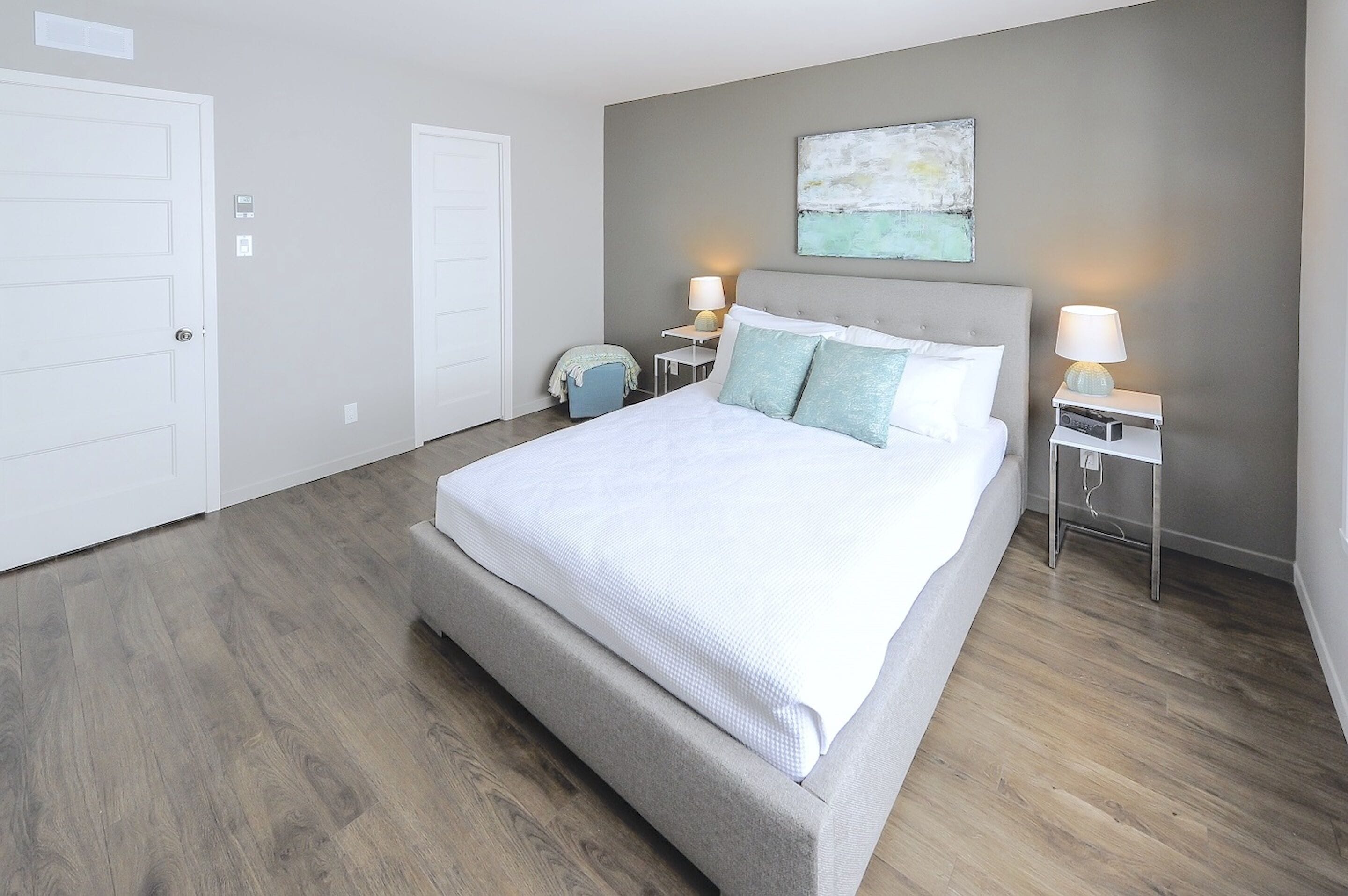 A bedroom with a large bed, two bedside tables with lamps, a small chair, and a painting on the wall.