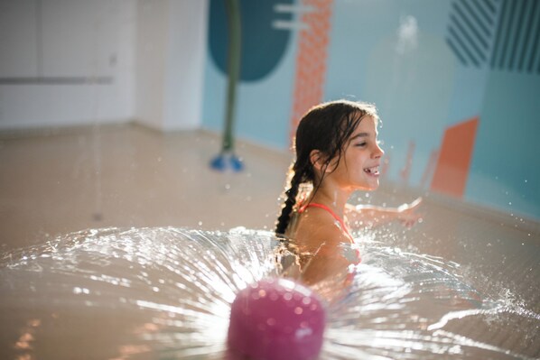 A child playing with water in a room with colorful walls and a visible mop in the background. - Auberge des Îles (Saint-Gedeon)