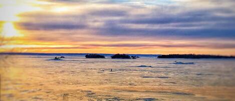 A sunset over a calm body of water with boats and a distant shoreline.