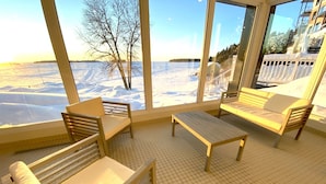 A room with a large window overlooking a snowy landscape. There are two wooden benches and a small table. - Auberge des Îles (Saint-Gedeon)