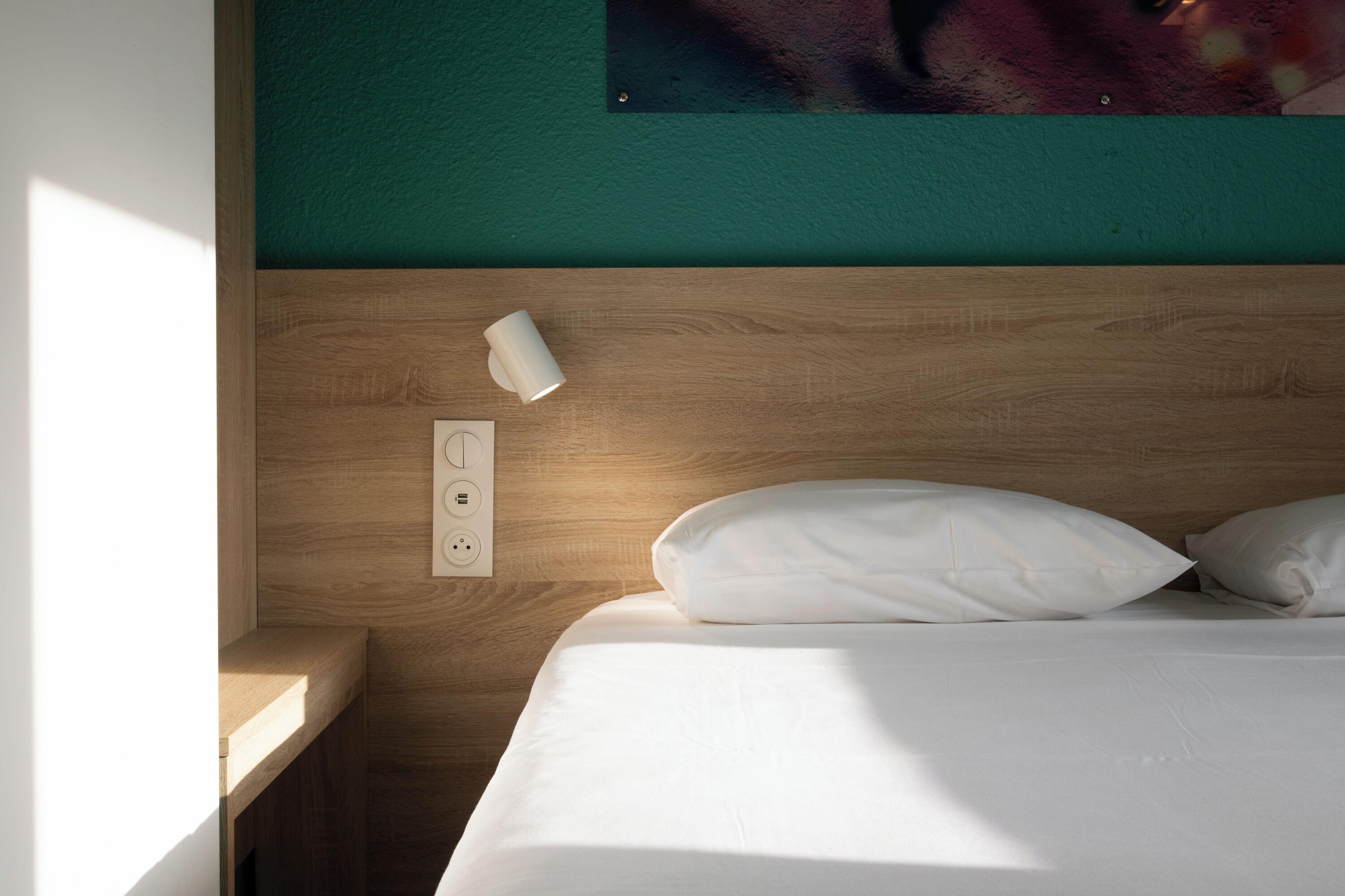 Una cama bien hecha con sábanas blancas, cabecera de madera y un enchufe en la pared.