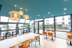 A spacious dining area with large windows, modern pendant lighting, and a variety of seating options. - Kyriad ECO - Dijon Sud Chenove (Chenove)