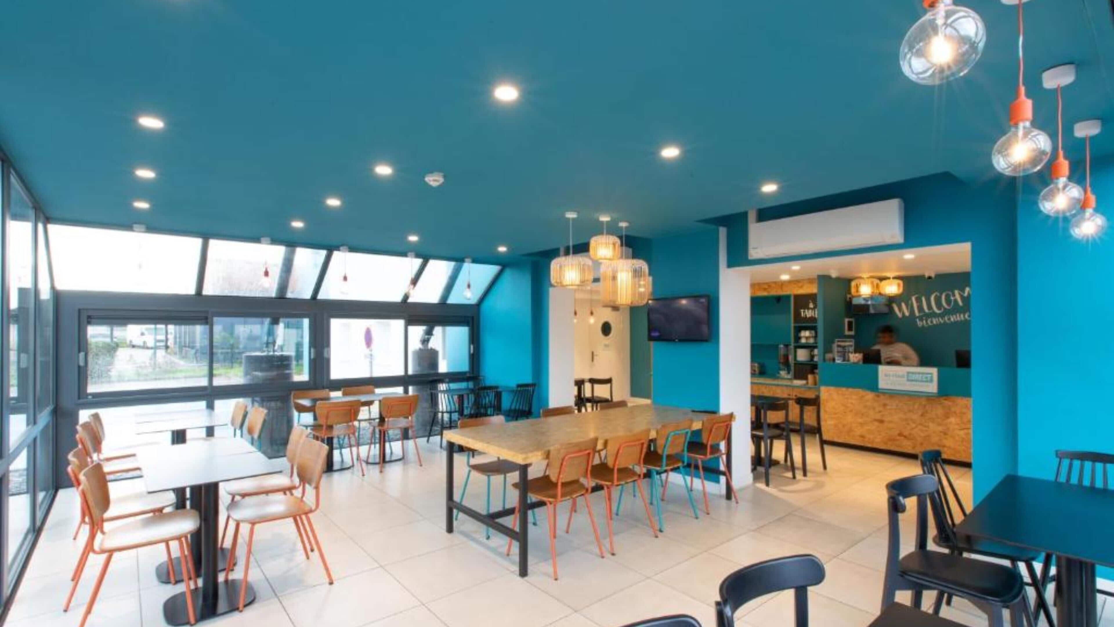 A modern restaurant with a blue color scheme, large windows, and a variety of seating options.