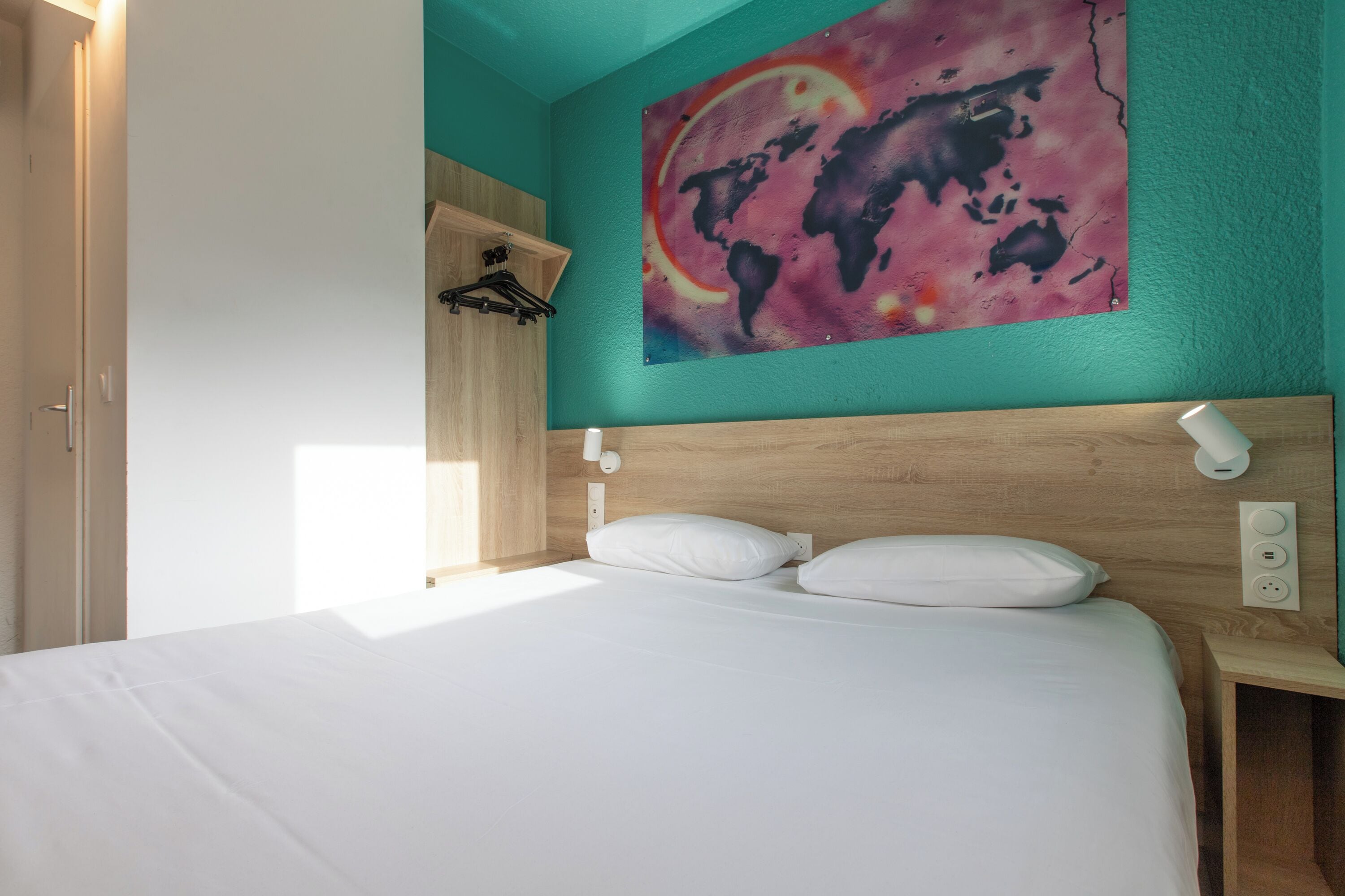 A bedroom with a bed, a wooden headboard, a world map artwork, and a nightstand with a lamp.