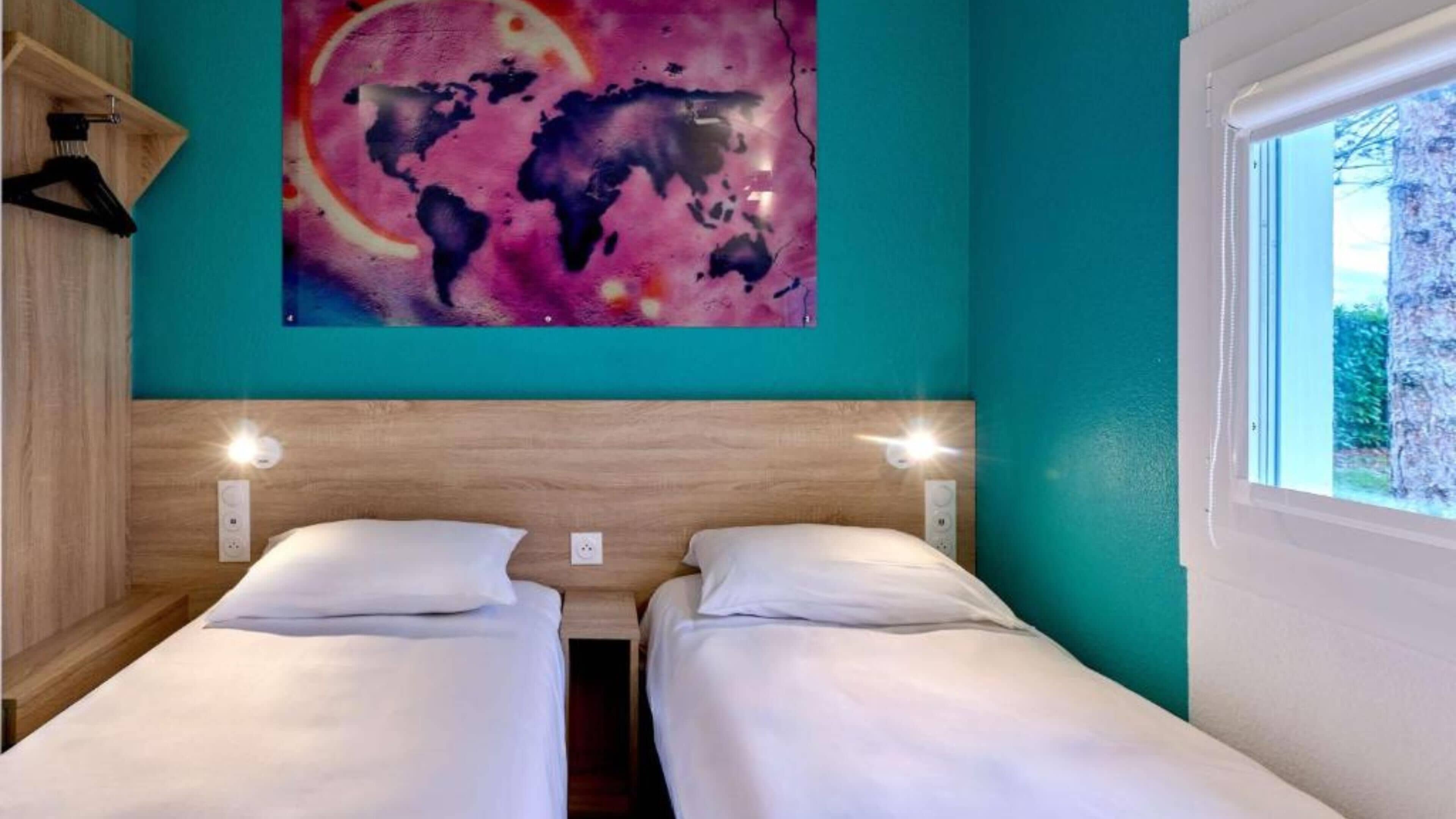 Una habitación con dos camas, un cuadro de un mapa mundial en la pared y una ventana con vistas a árboles.