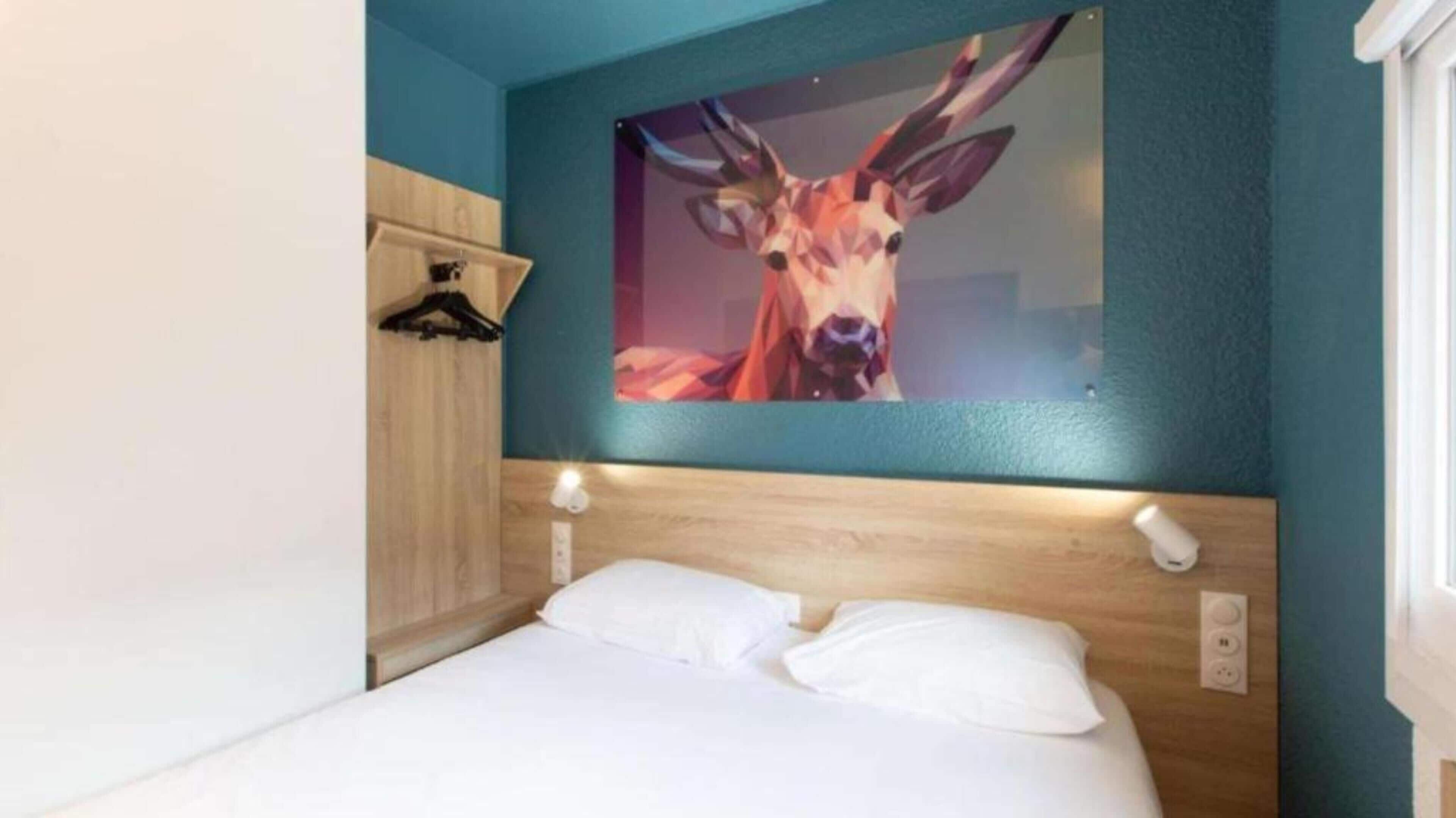 A bedroom with a bed, a wooden headboard, a wall-mounted picture of a deer, and a light switch.