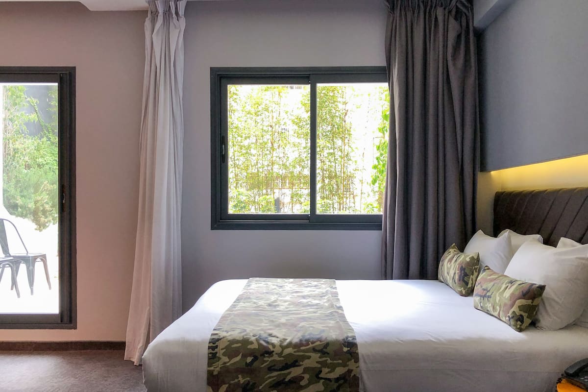 A bedroom with a bed, a window with curtains, and a view of greenery outside.