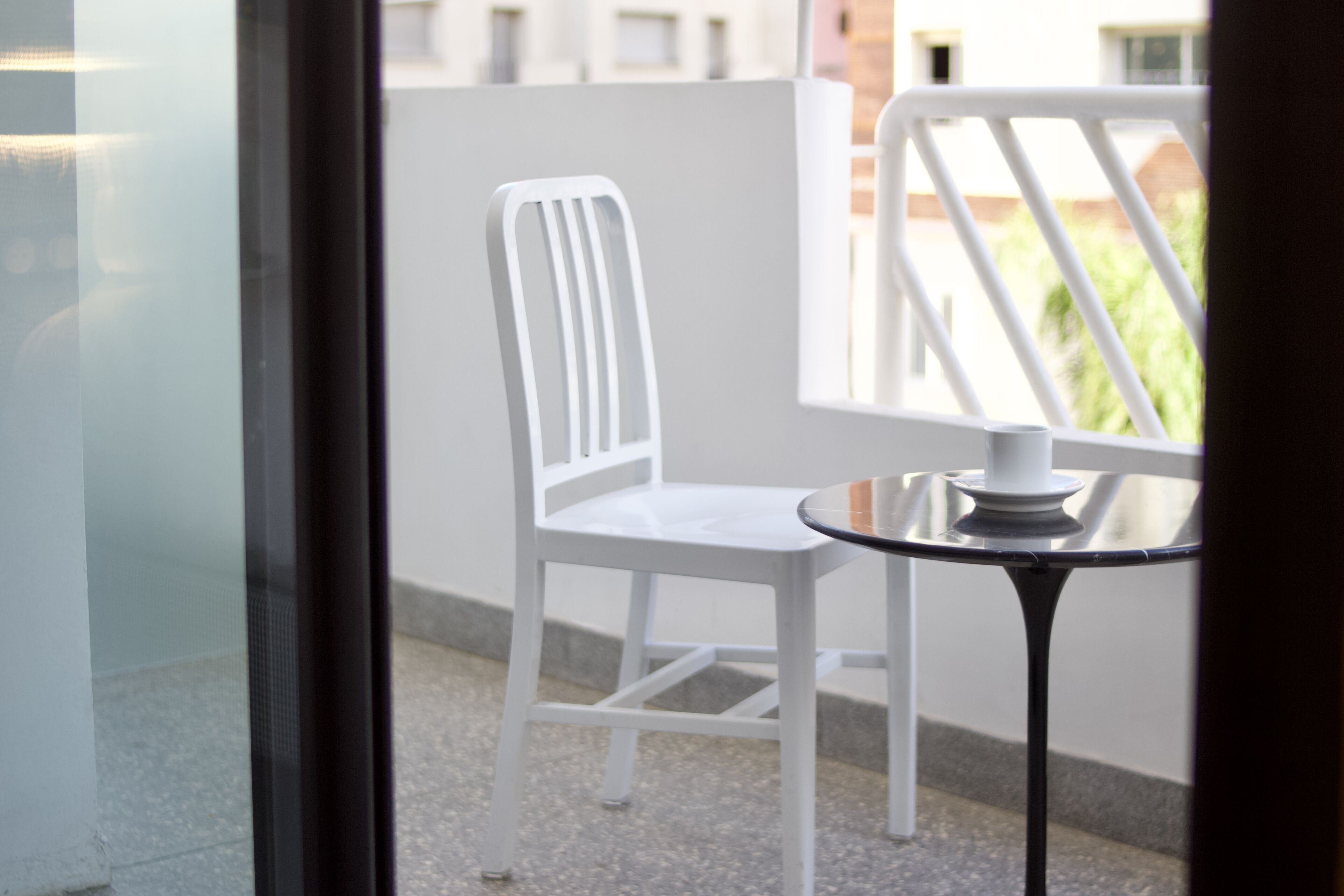 Une chaise blanche et une petite table sur un balcon doté d’une balustrade.