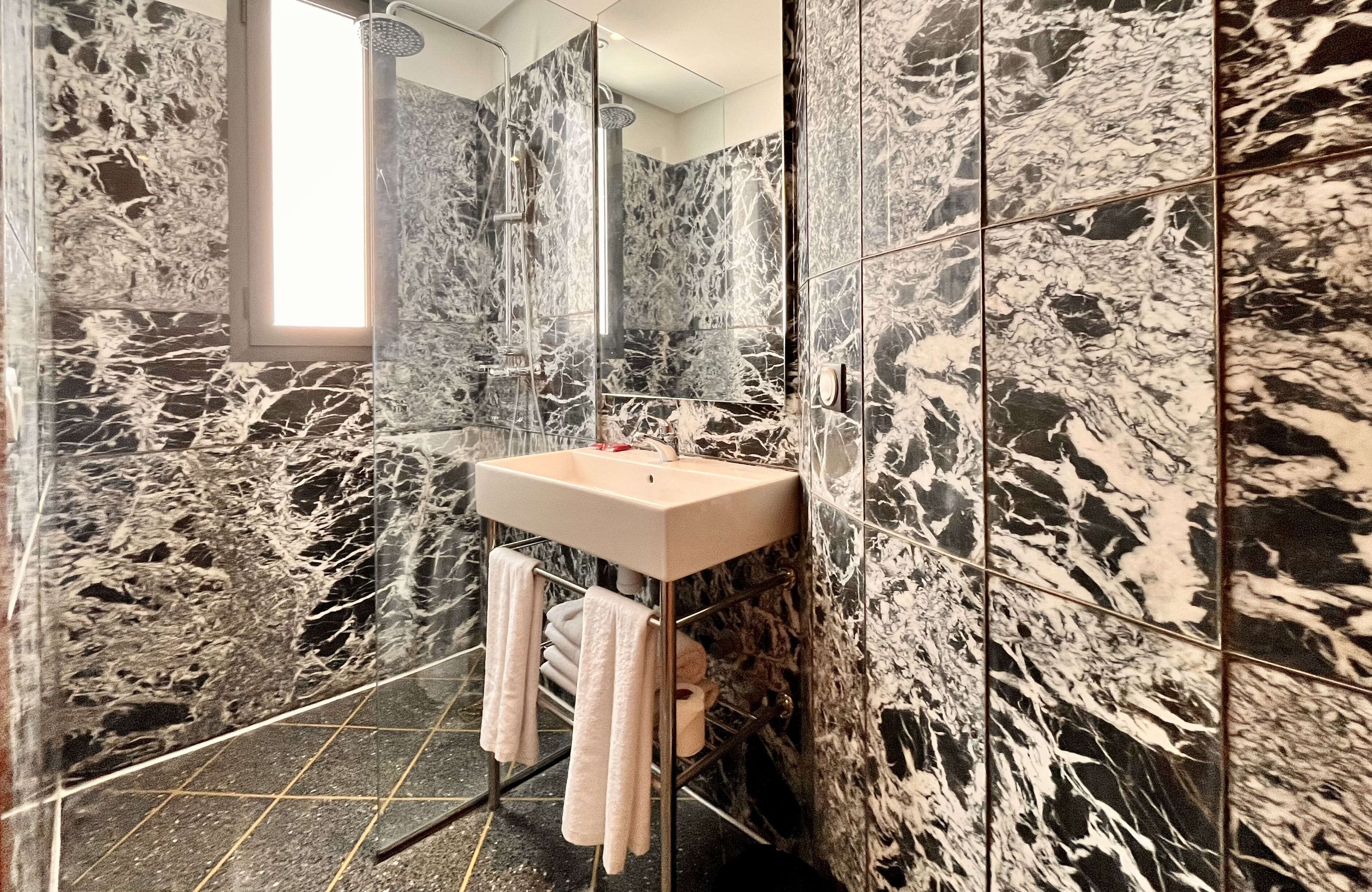 A modern bathroom with a marble wall, a glass shower enclosure, and a sink with towels.