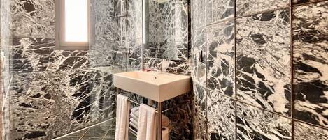 A modern bathroom with a marble wall, a glass shower enclosure, and a sink with towels.