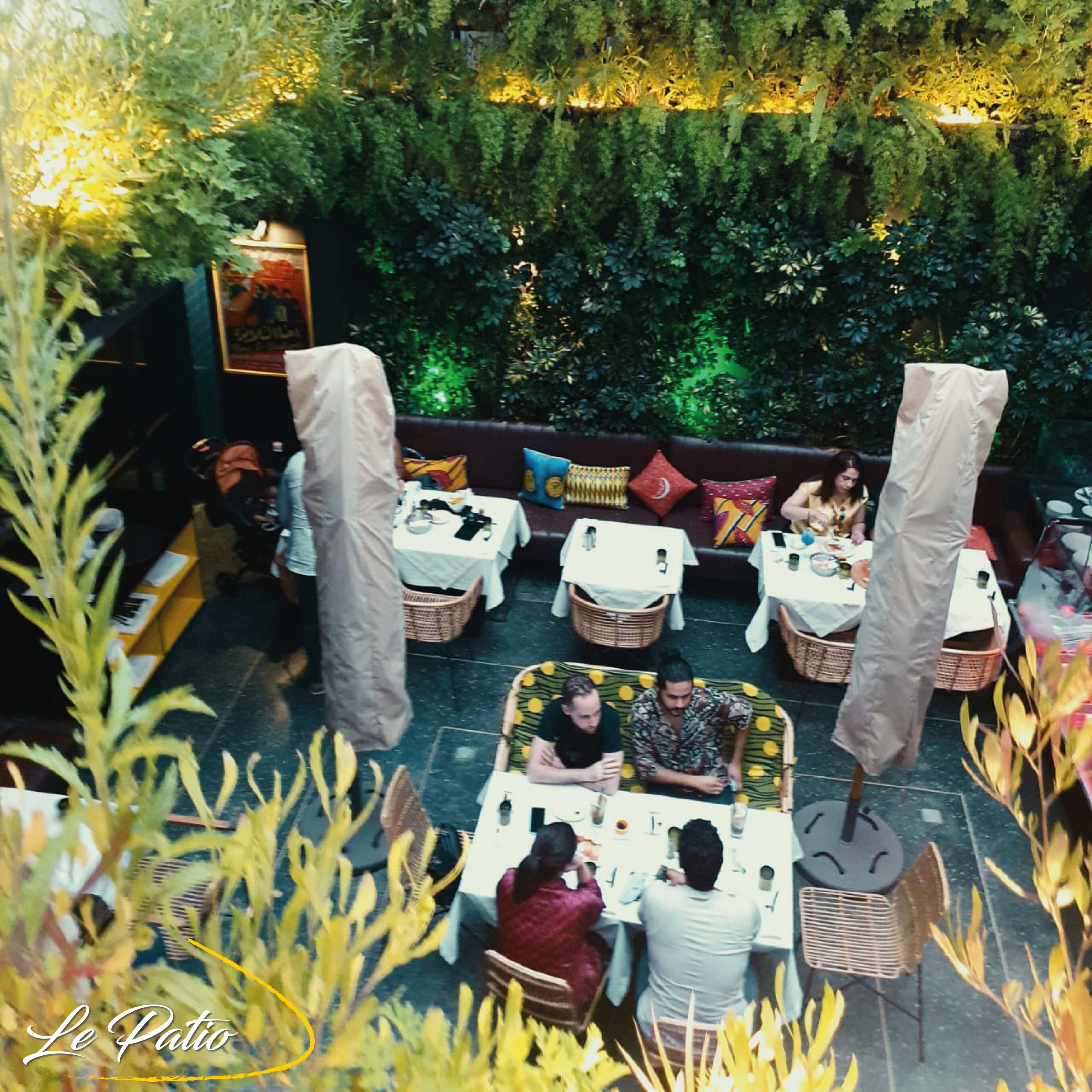 An outdoor dining area with tables and chairs, surrounded by greenery and a wall of plants.