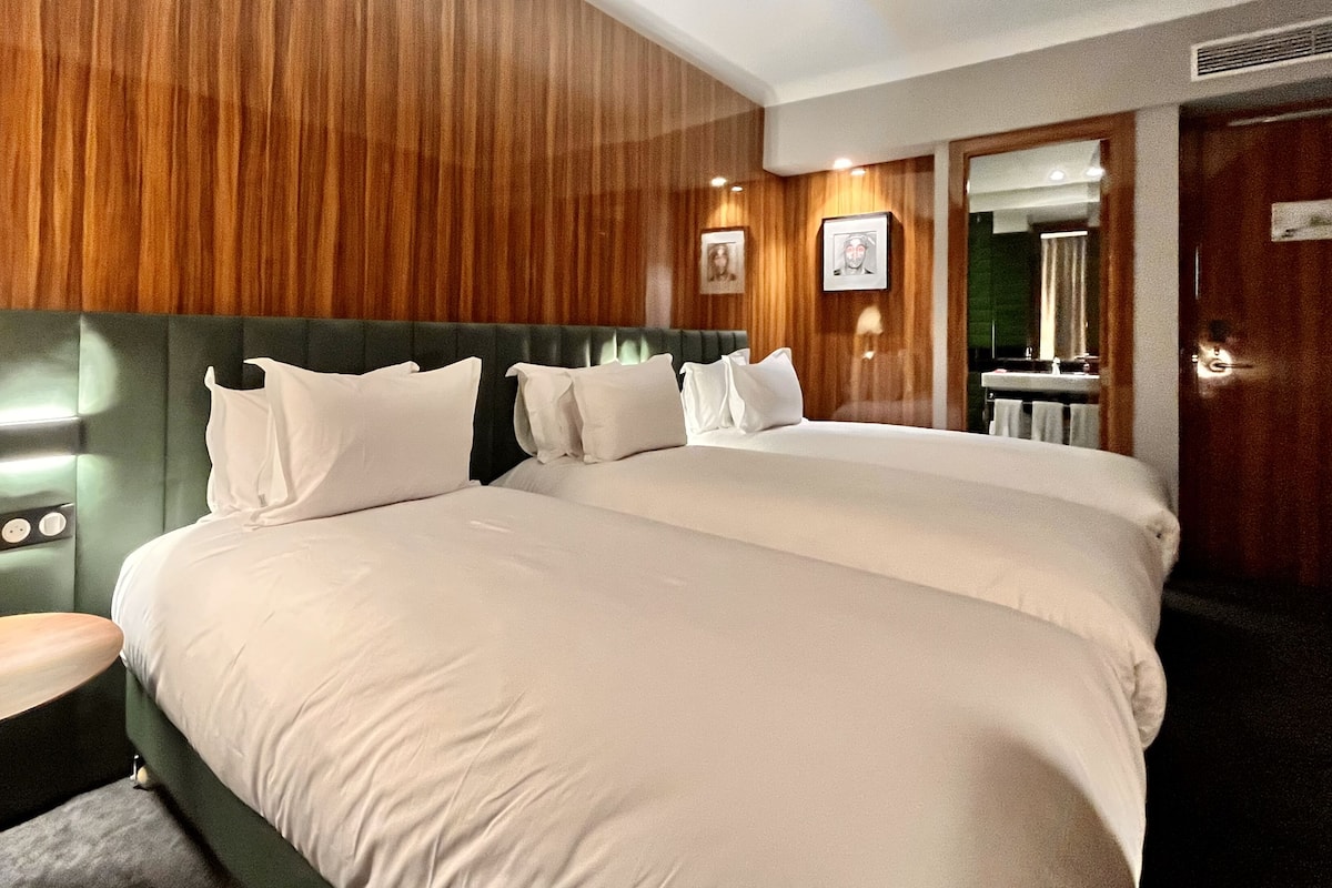 A hotel room with a large bed, a bedside table, a mirror, and wooden paneling on the walls.