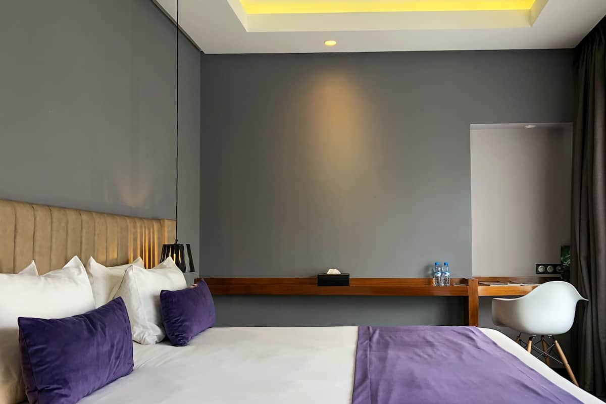A hotel room with a bed, pillows, a bedside table with a tissue box, a water bottle, and a chair.