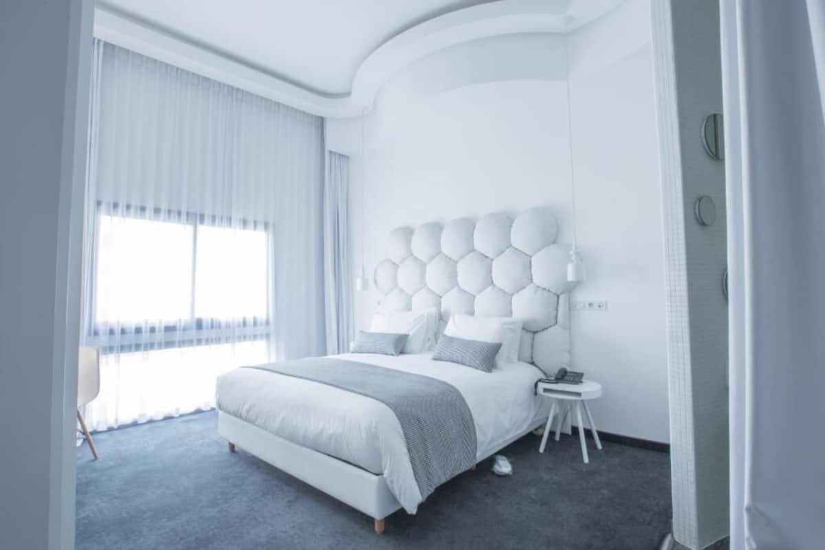 A modern bedroom with a large bed, a white headboard, and a small bedside table.