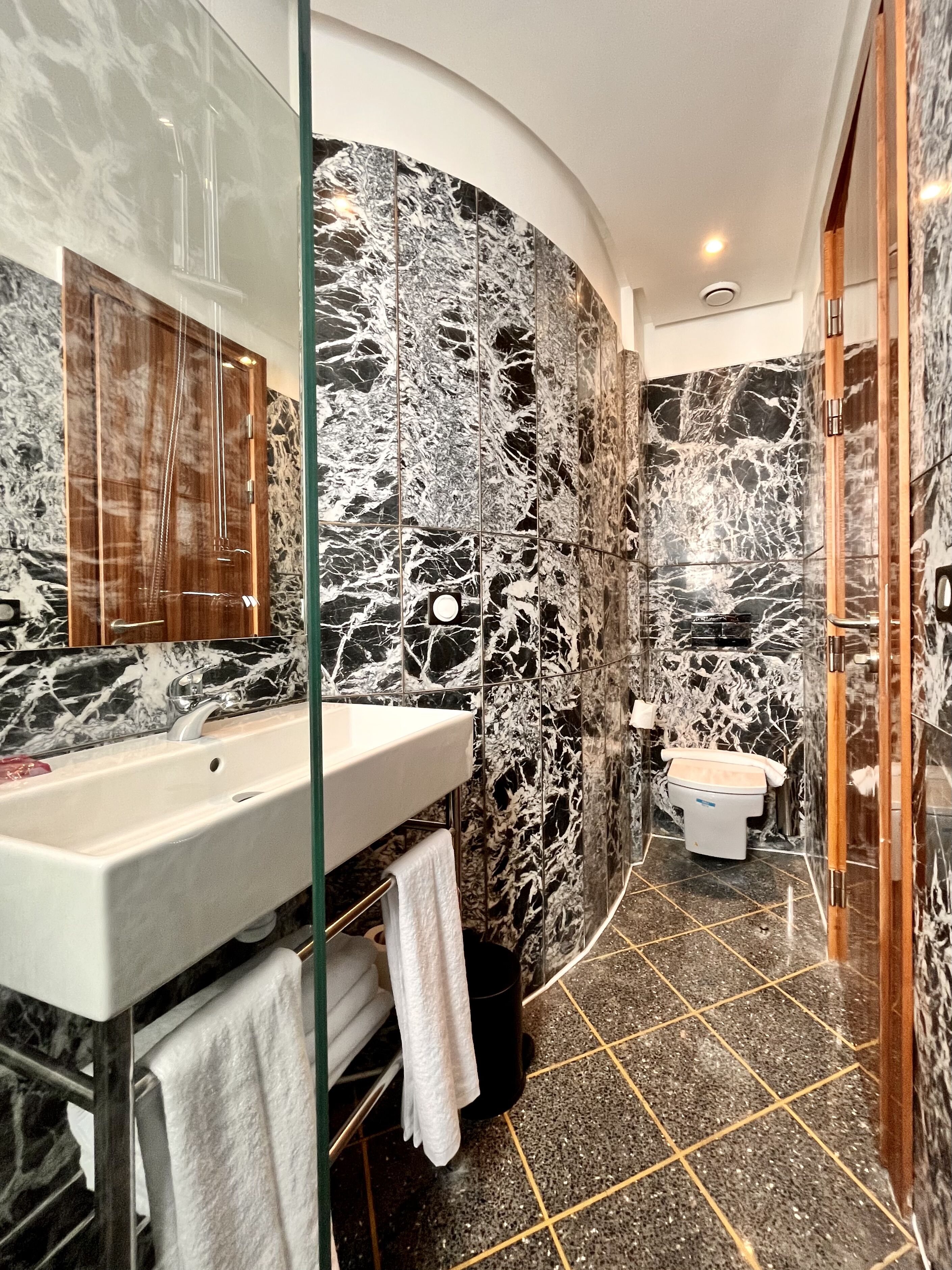 Une salle de bain moderne avec un mur en marbre, une douche en verre et un lavabo blanc.