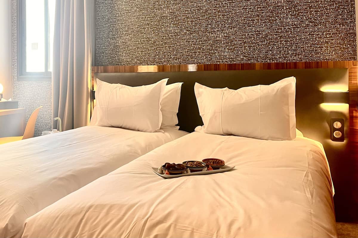A hotel room with two beds, a wall with a textured pattern, and a tray of food on the bed.