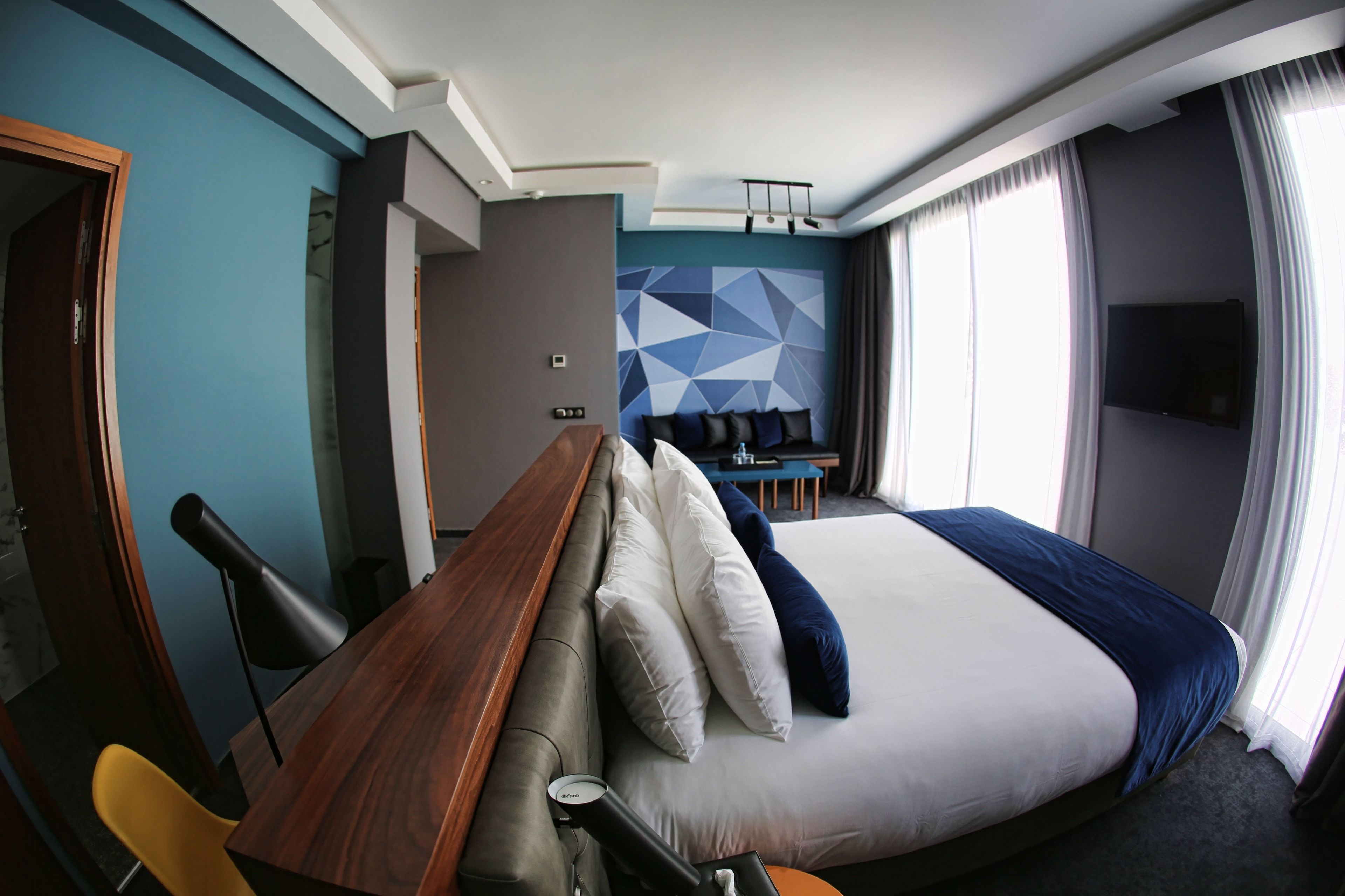 A modern hotel room with a large bed, a wooden desk, and a seating area with chairs.
