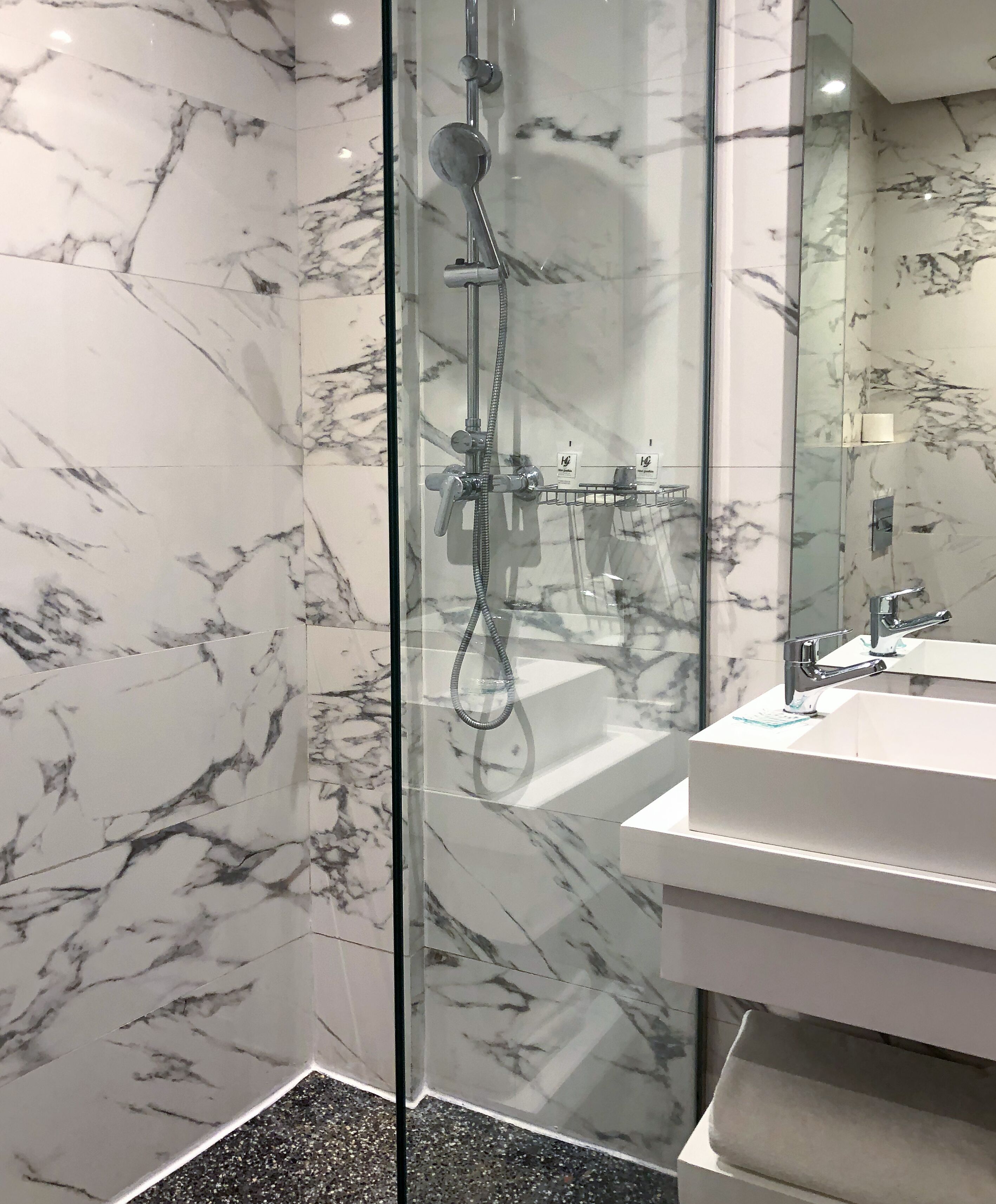Ein modernes Badezimmer mit einer gläsernen Duschkabine, einer weißen Marmor-Spritzschutzwand und einem weißen Waschbecken mit chromfarbenem Wasserhahn.