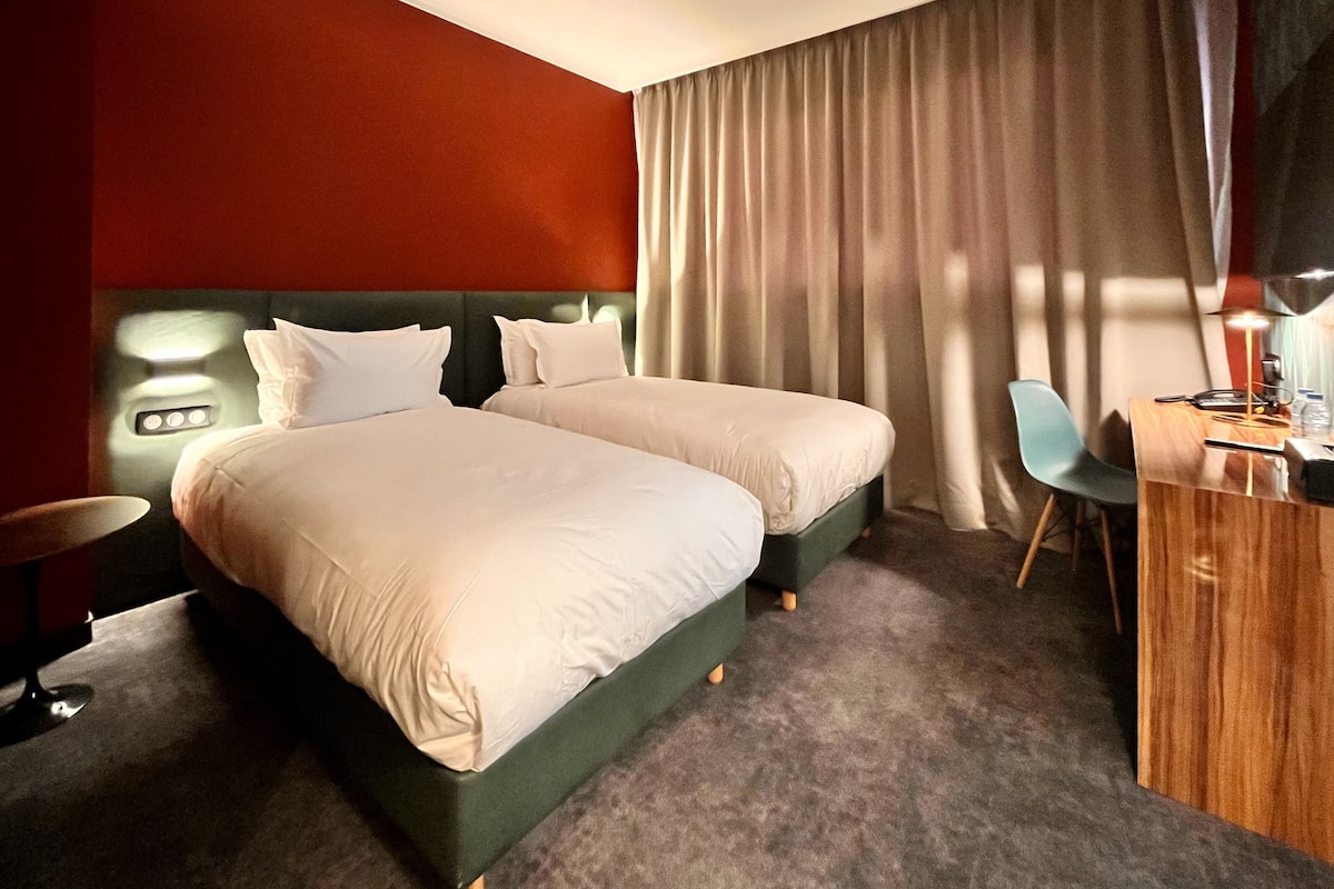 A hotel room with two beds, a desk, a chair, and a small table.